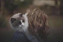 A girl holding her white cat behind her head