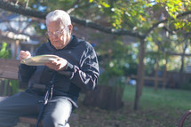 an elderly man eating on a bench outdoors 