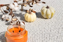 pumpkins, orange candle, and cotton sprays on a gray blanket 