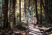 twin girls walking on a path through a forest 
