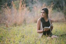 A young woman sitting outside in the grass and reading.