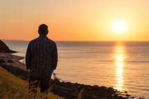 a man standing along a shore at sunset 