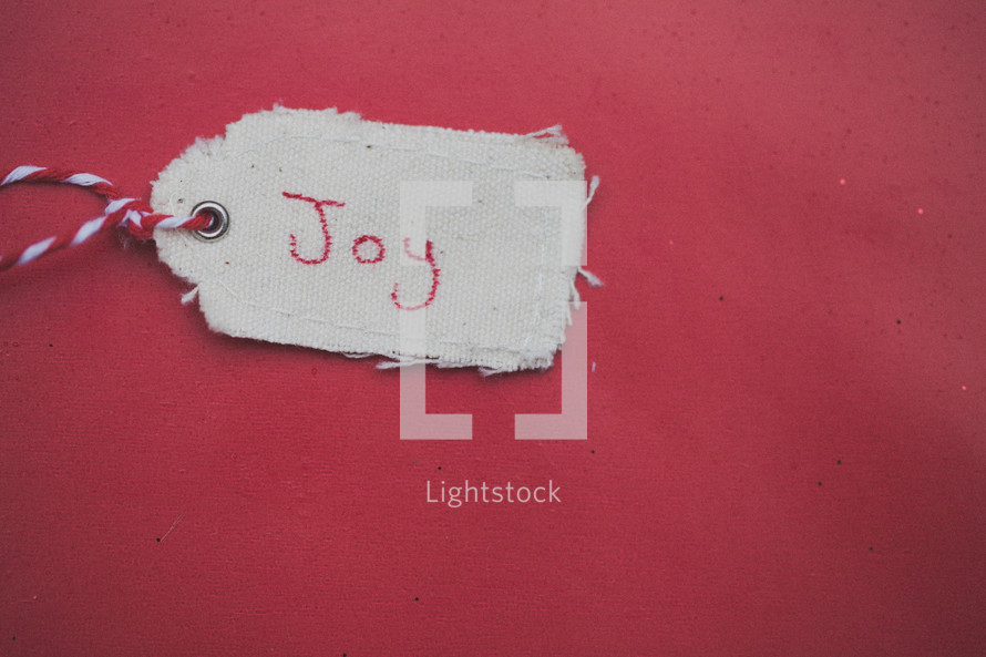 A Christmas gift tag reading "Joy," on a red background.