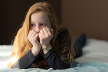 teen girl lying on a bed with her hands over her face thinking 