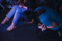 women kneeling on the floor surrendering to God at a worship service 