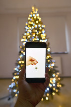 Image of a hand holding a bell on a phone in front of a Christmas tree