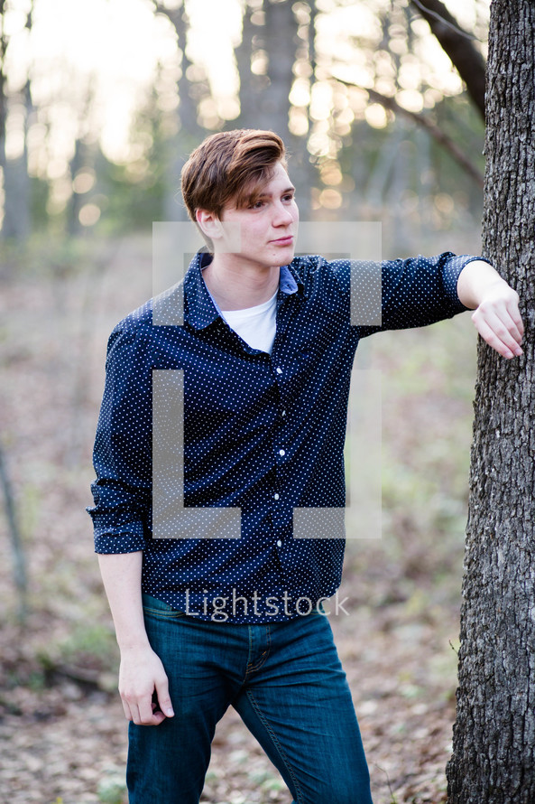 a young man leaning against a tree 