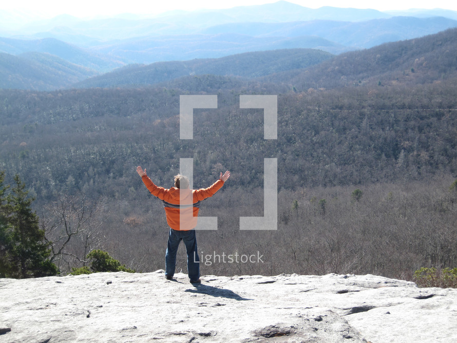 a man standing on a mountain top with raised hands 
