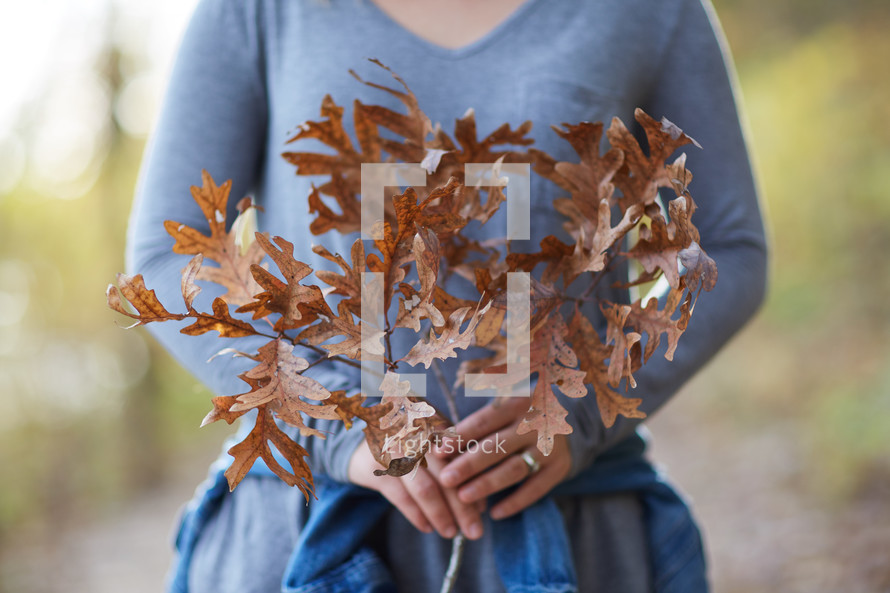 a woman holding a branch of brown fall leaves 