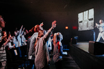 audience with raised hands in front of a stage 