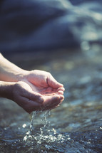 cupped hands gathering water from a stream