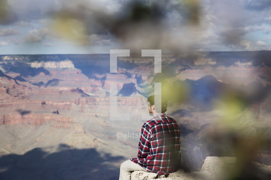man sitting at the edge of a canyon cliff 