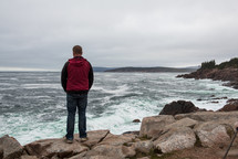 a man standing on a rocky shore looking out into the ocean 