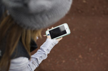 A woman in a winter hat looks at her cell phone.