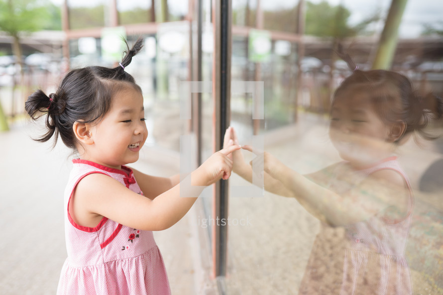 toddler looking at her reflection in a window 