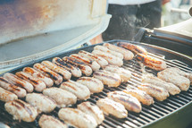 Hotdogs cooking on an outdoor barbecue grill.
