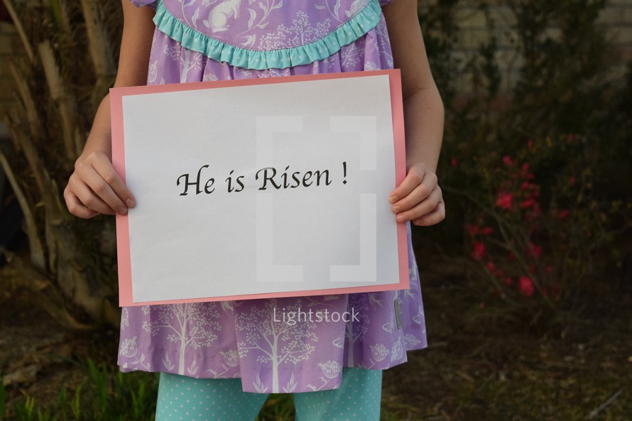 A little girl holding a He is Risen sign 