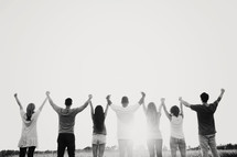 group of young adults standing holding raised hands outdoors with backs to the camera