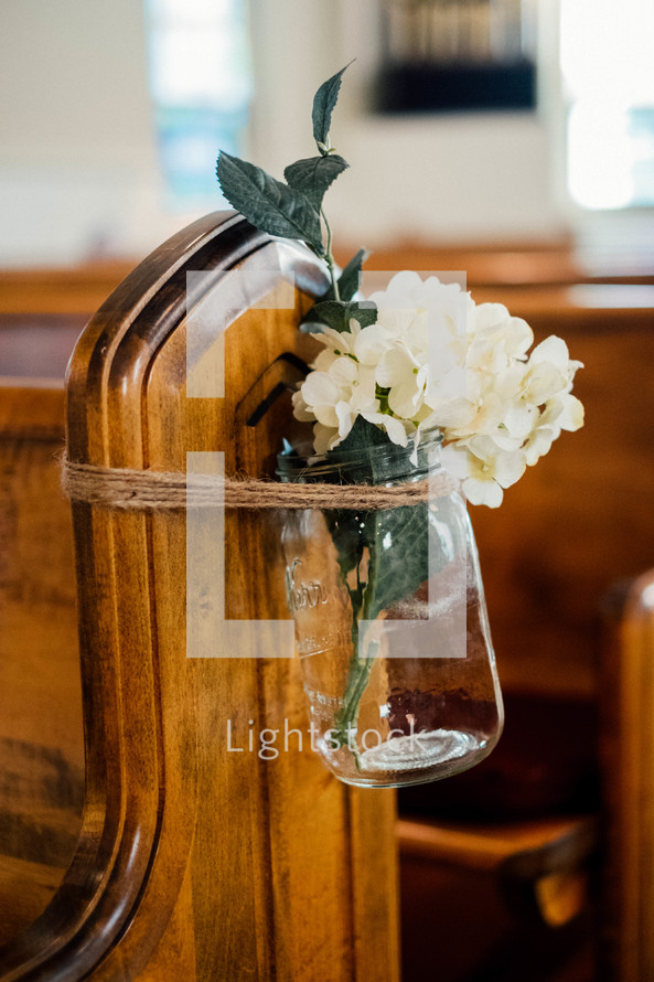 flowers in a mason jar tied around a church pew 