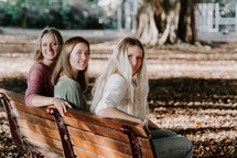 three women sitting on a park bench 
