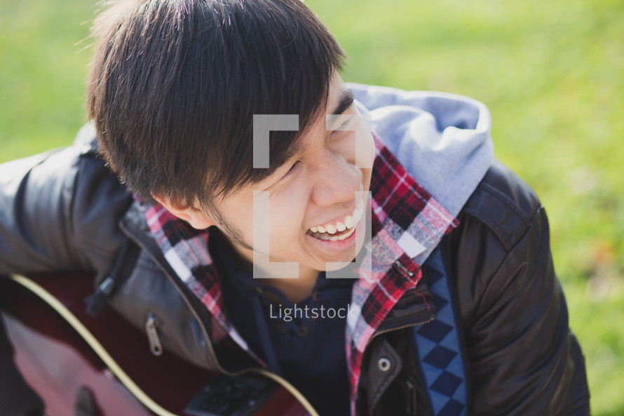 a teen boy playing a guitar outdoors 