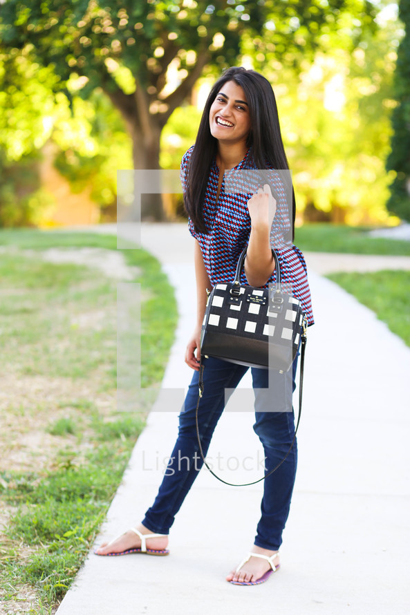 young woman with a purse standing on a sidewalk 