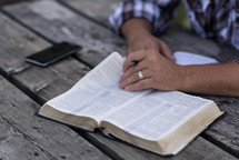 a man reading a Bible at a picnic table outdoors 