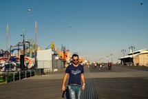 a man walking on a boardwalk beside an amusement park 