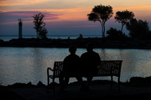 silhouette of a man and woman looking out at lake water at sunset