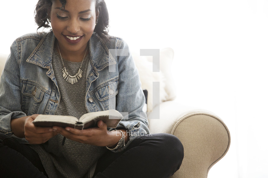 A woman sitting on couch reading a Bible 