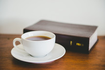 Cup of coffee with a Bible on a wooden table.