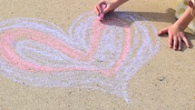 a little girl drawing a Valentine's purple and pink heart on concrete in sidewalk chalk 