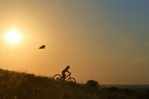 silhouette of a child on a bike with a kite at sunset 