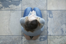 Aerial view of woman sitting on her knees on tiles in prayer.