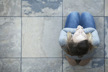 Aerial view of a woman sitting on her knees on tile in prayer.