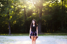 a teen girl standing under sunlight outdoors 