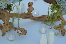 candles, driftwood, and hydrangeas as a centerpiece on a table for a beach themed wedding 