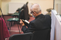 a senior man wearing a face mask reading a Bible at church 