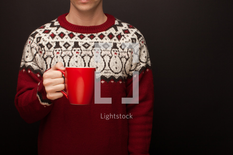 a man in a Christmas sweater holding a mug 
