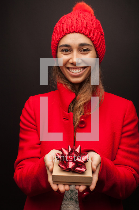 a woman in a red trench coat holding a gift box at Christmas 