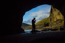silhouette of a man in prayer at the entrance of a cave 