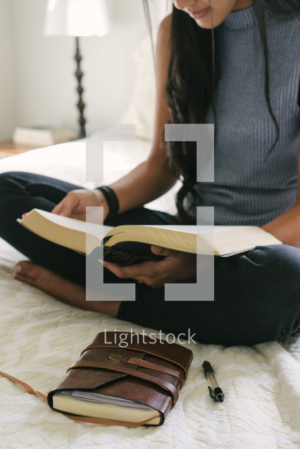 young woman reading a Bible on her bed 