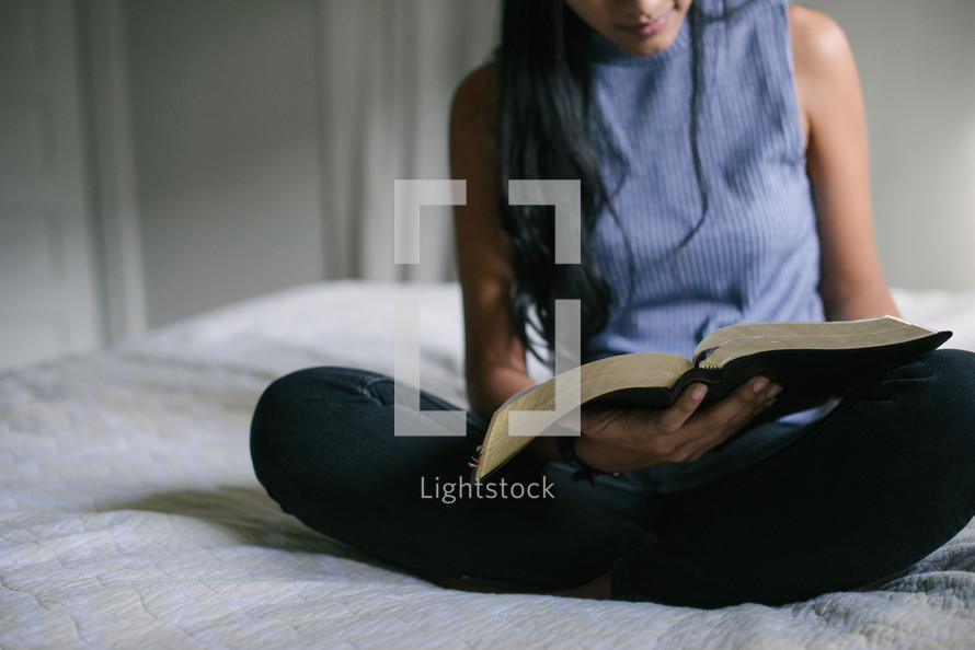 A teen girl sitting on her bed and reading the Bible.