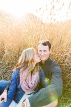 woman kissing a man on the cheek while sitting in a field