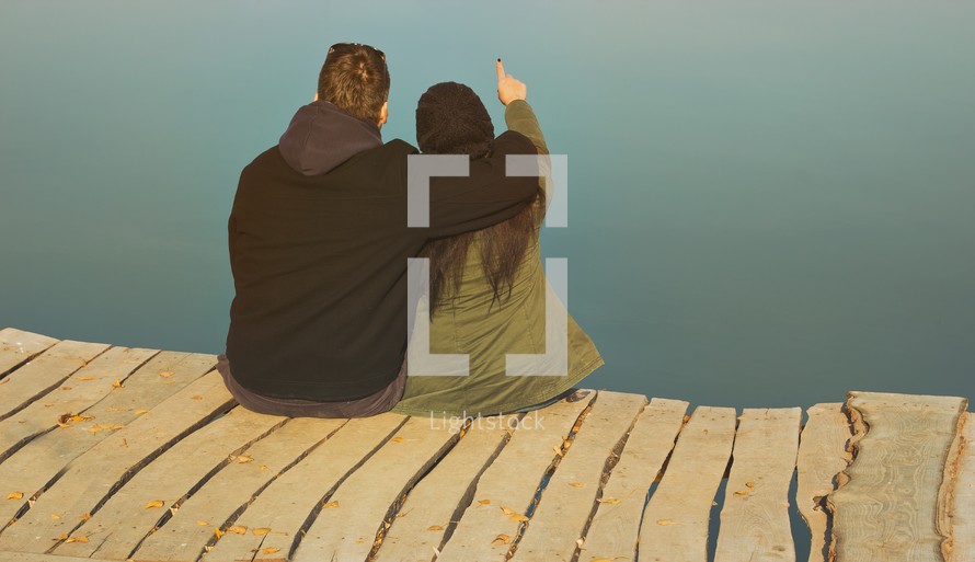 a couple sitting at the end of a dock pointing 