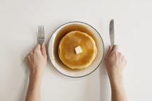 person with fork and knife in hand with pancakes on a plate. Ready for breakfast.