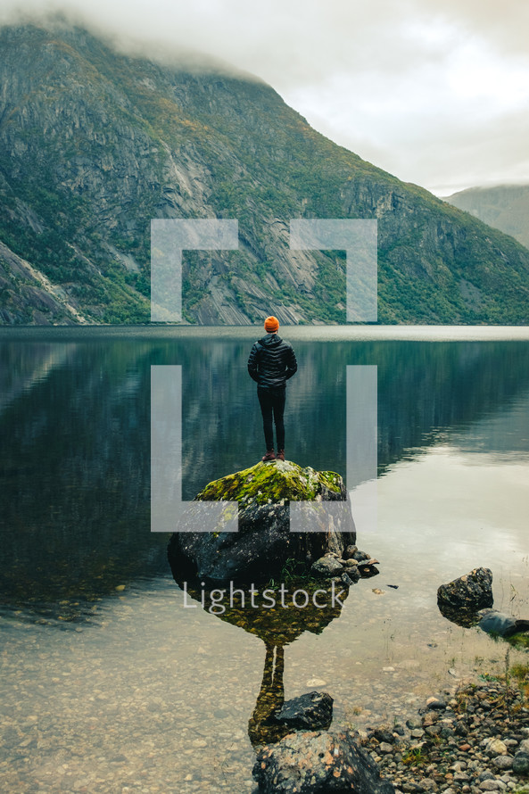a man standing on a rock in the middle of a lake taking in the views