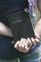 Teen girl holding Bible behind her back.