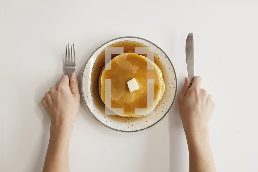 person with fork and knife in hand with pancakes on a plate. Ready for breakfast.