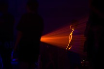 a man standing in the beam of a red spotlight while standing in an audience 